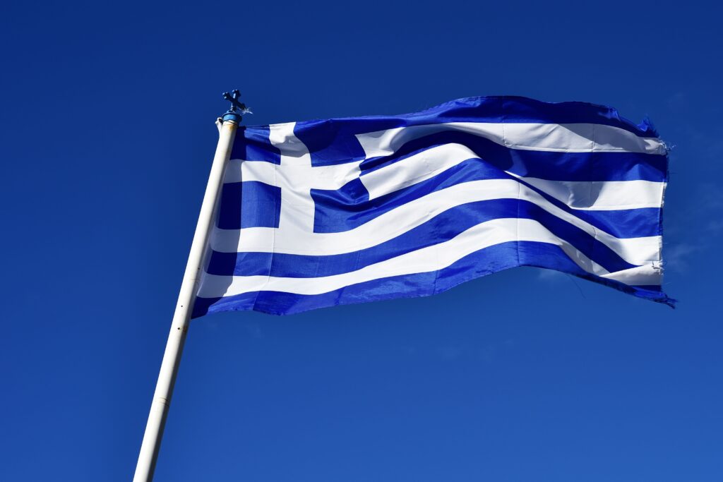 The Greek national flag waves against a clear blue sky, representing national pride and symbolism.
